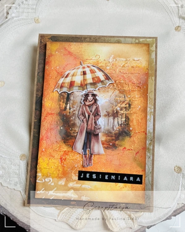 Kartka handmade „Jesieniara” z jesienną ilustracją kobiety z parasolką w ciepłych odcieniach pomarańczu, żółci i czerwieni. Projekt sezonowy od Scrapstacja.