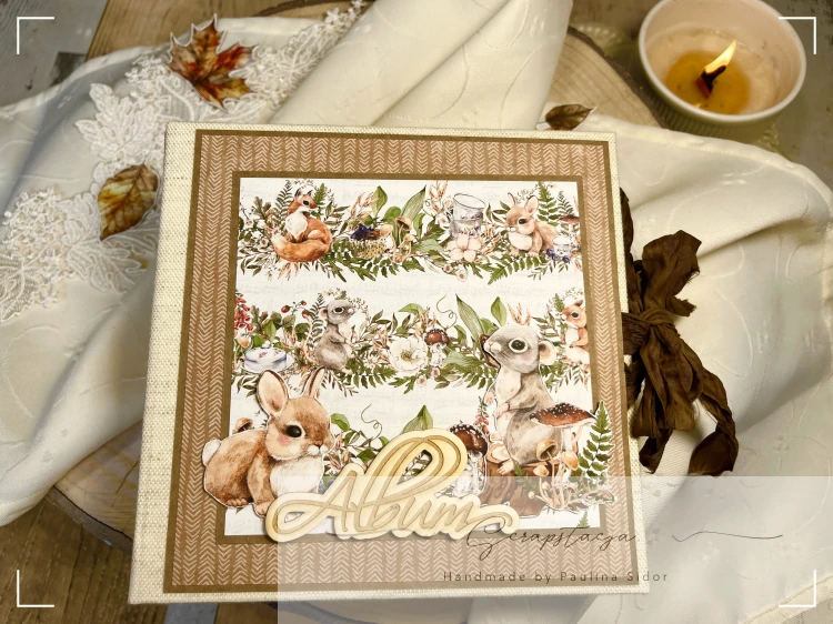 Zdjęcie przedstawia okładkę albumu wykonanego ręcznie metodą scrapbookingu w leśnym klimacie. Okładkę stanowi grafika z leśnymi zwięrzątkami i dużym napisem Album. Album zamykany na wstążkę gnieciuszkę.